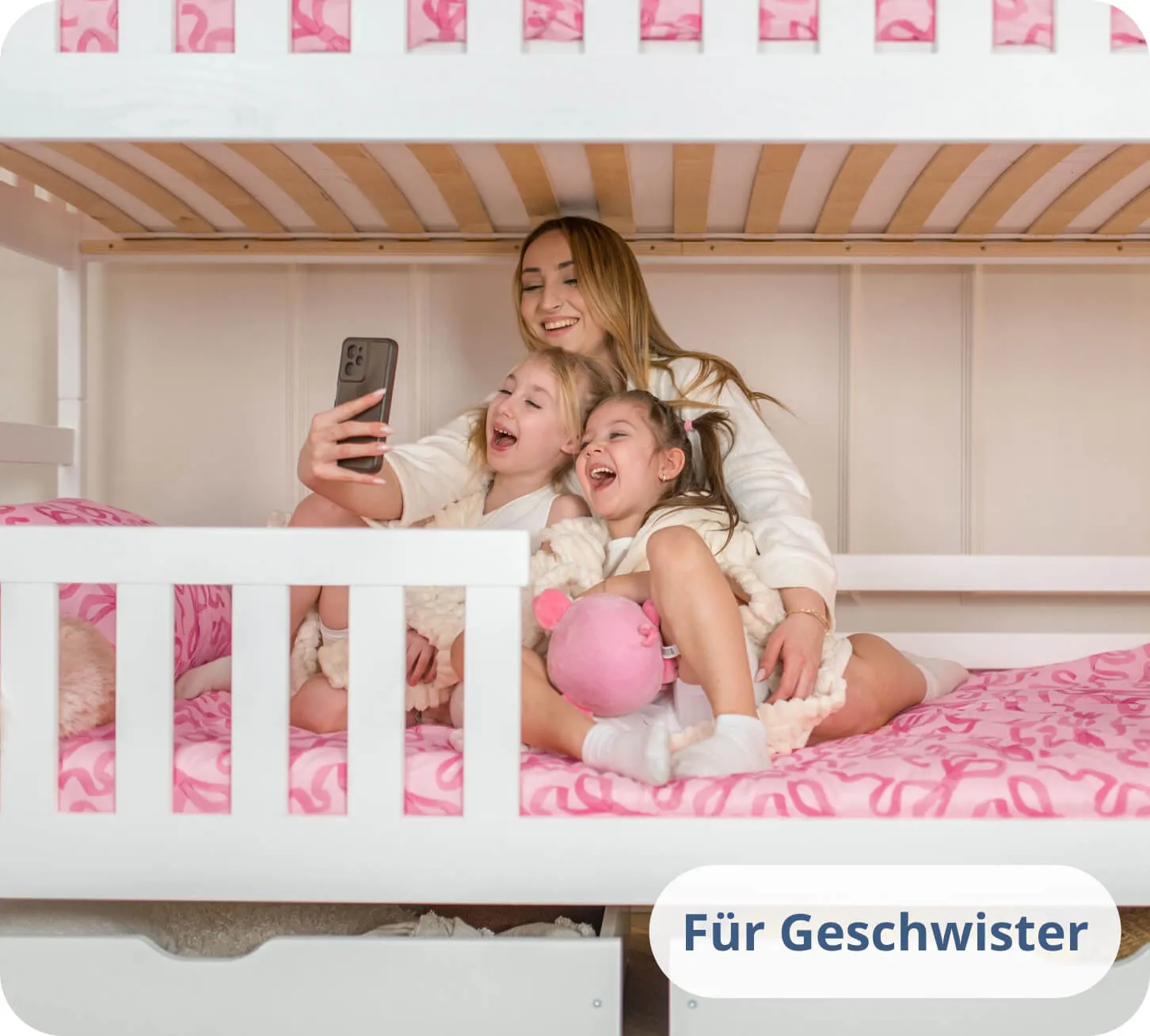 Zwei Mädchen und eine Frau lachen in ein Telefon auf einem weißen Etagenbett.